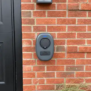 Electric car charger fitted beside a door on a brick wall